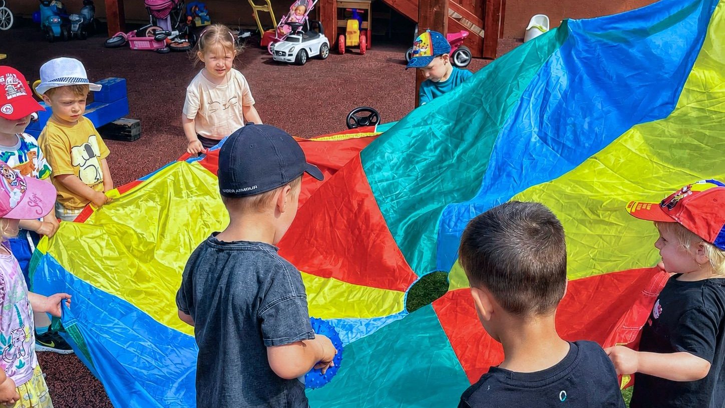 Deti sa spoločne hrajú s farebným padákom na dvore jaslí BIBO